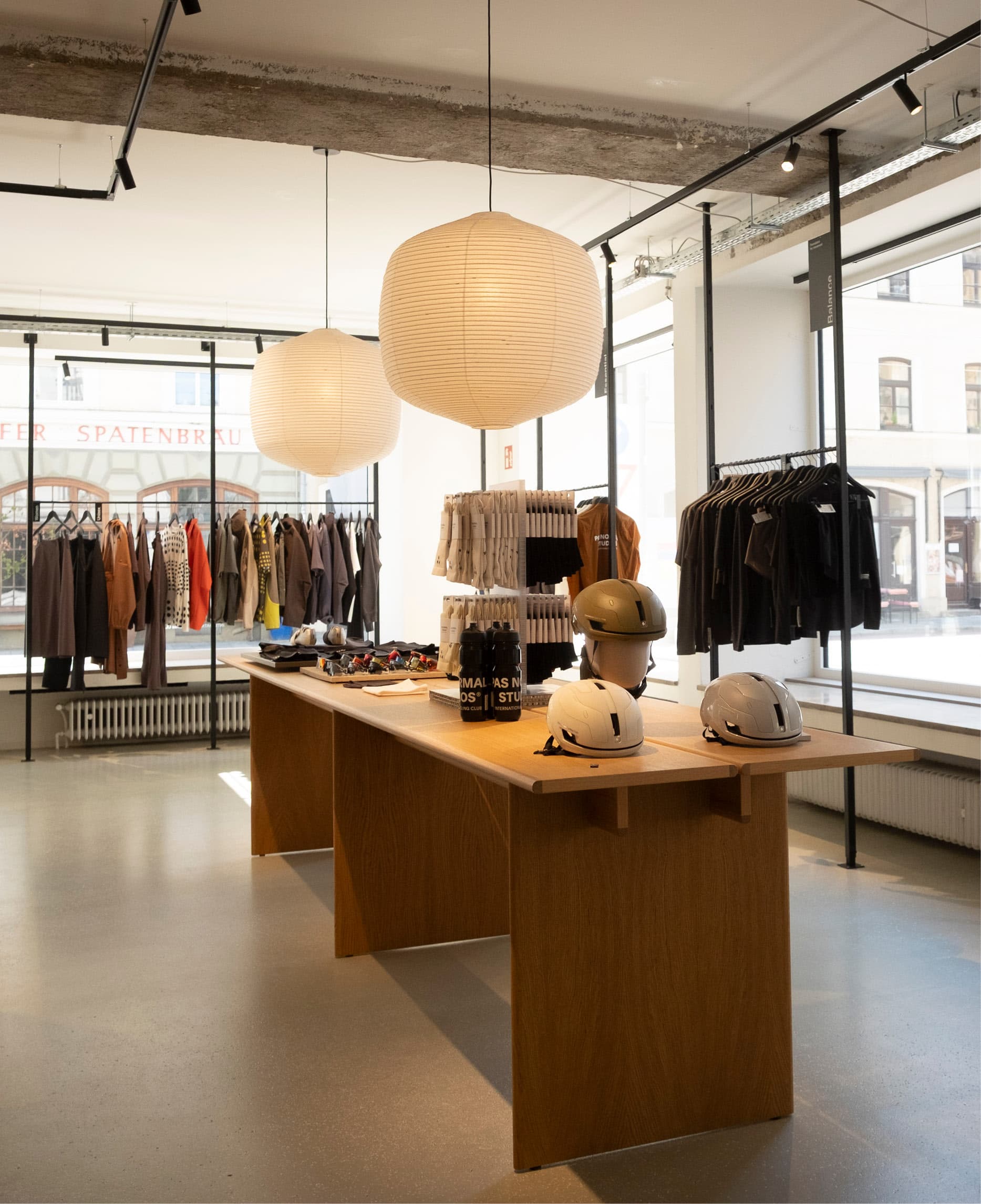 Concept Store mit hellen Kugelleuchten, Holztisch und Kleiderstangen