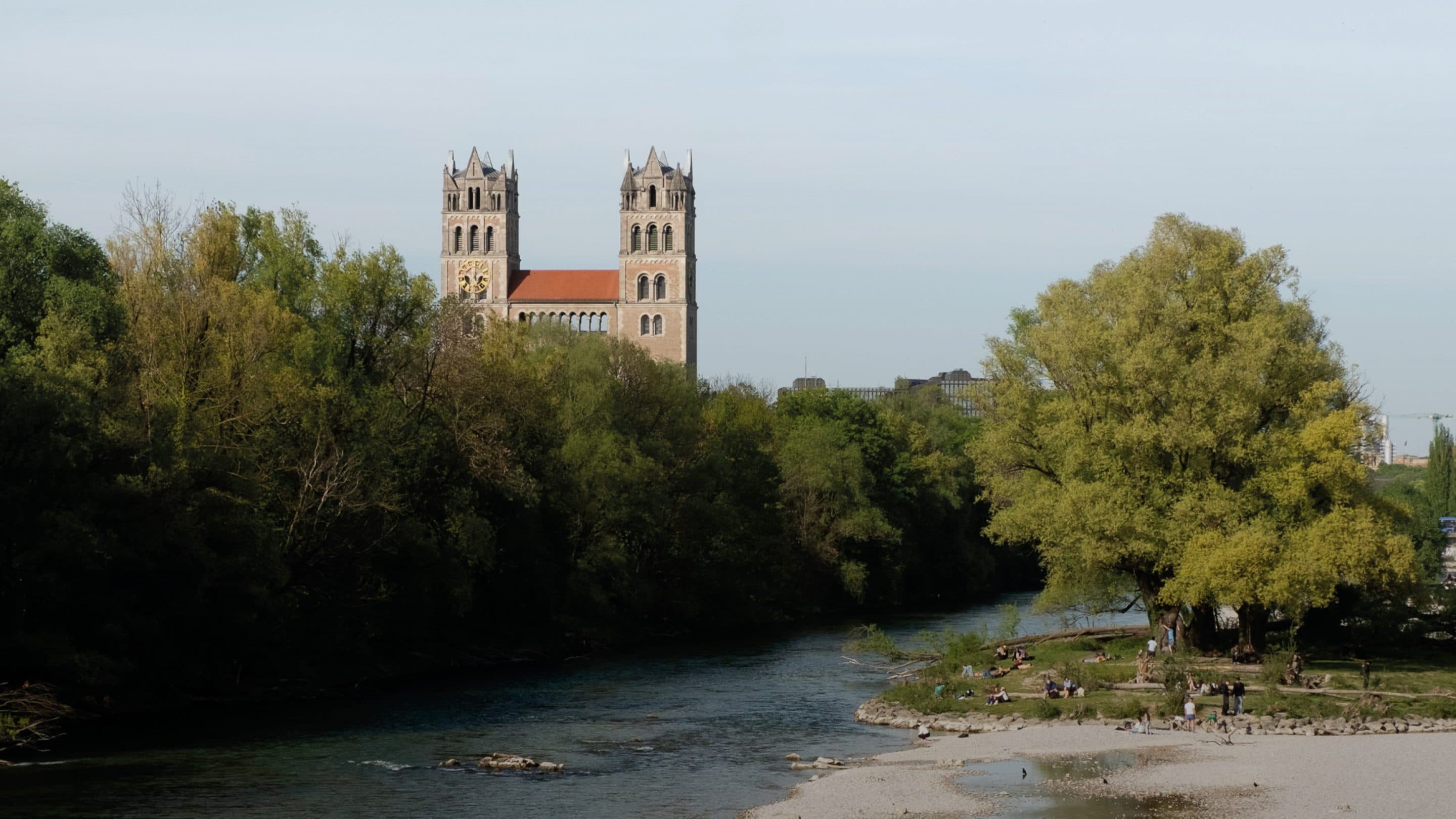 Die Isar mit Kiesbank und Auwald, dahinter die Türme von St. Maximilian