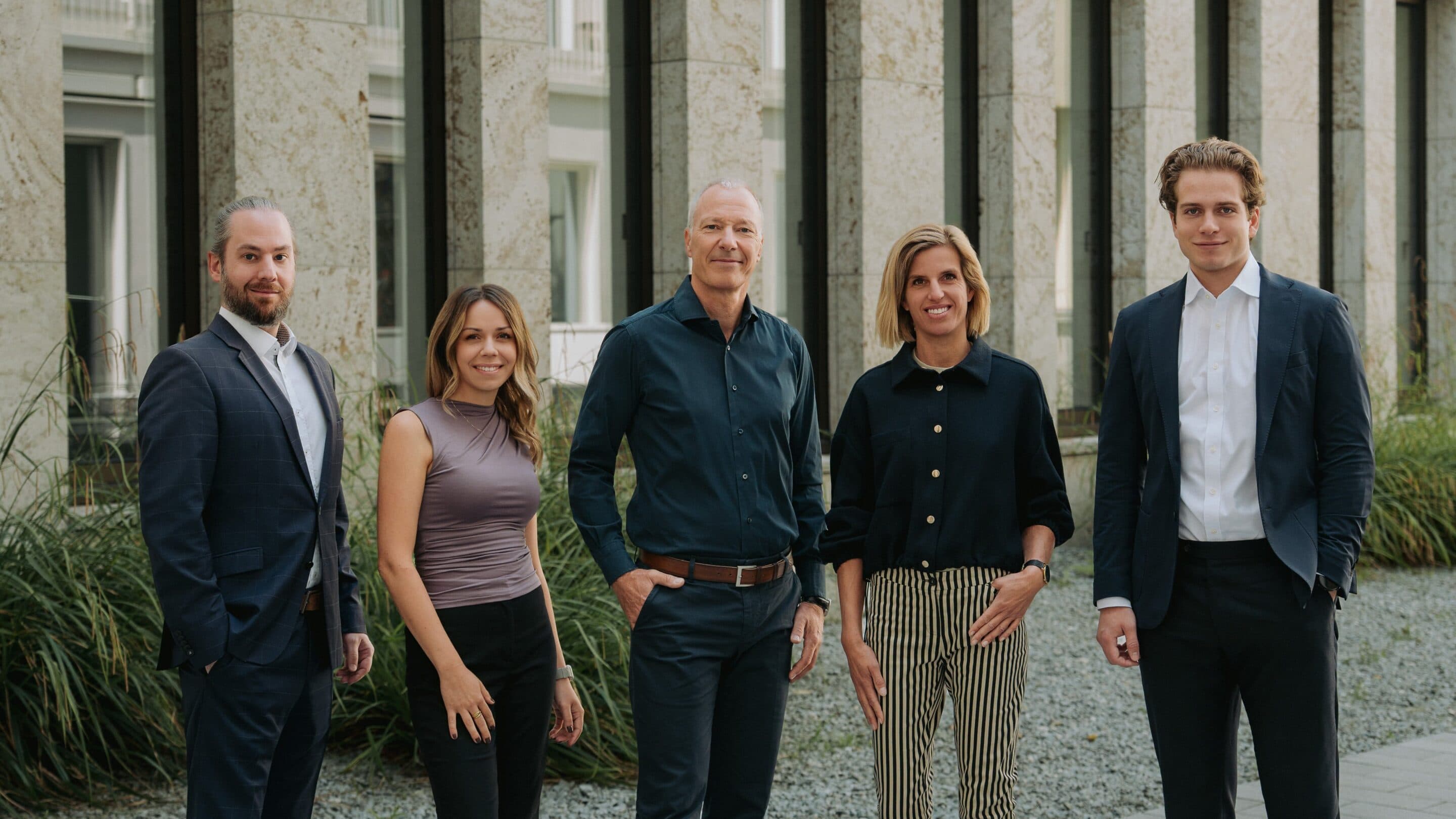 Das fünfköpfige Team der INVENTIO Projectpartner GmbH vor einer Natursteinfassade mit Gräsern